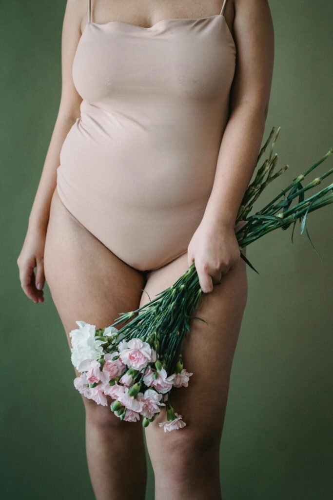 Persona con un body beige sosteniendo un ramo de flores blancas y rosas ante un fondo verde.