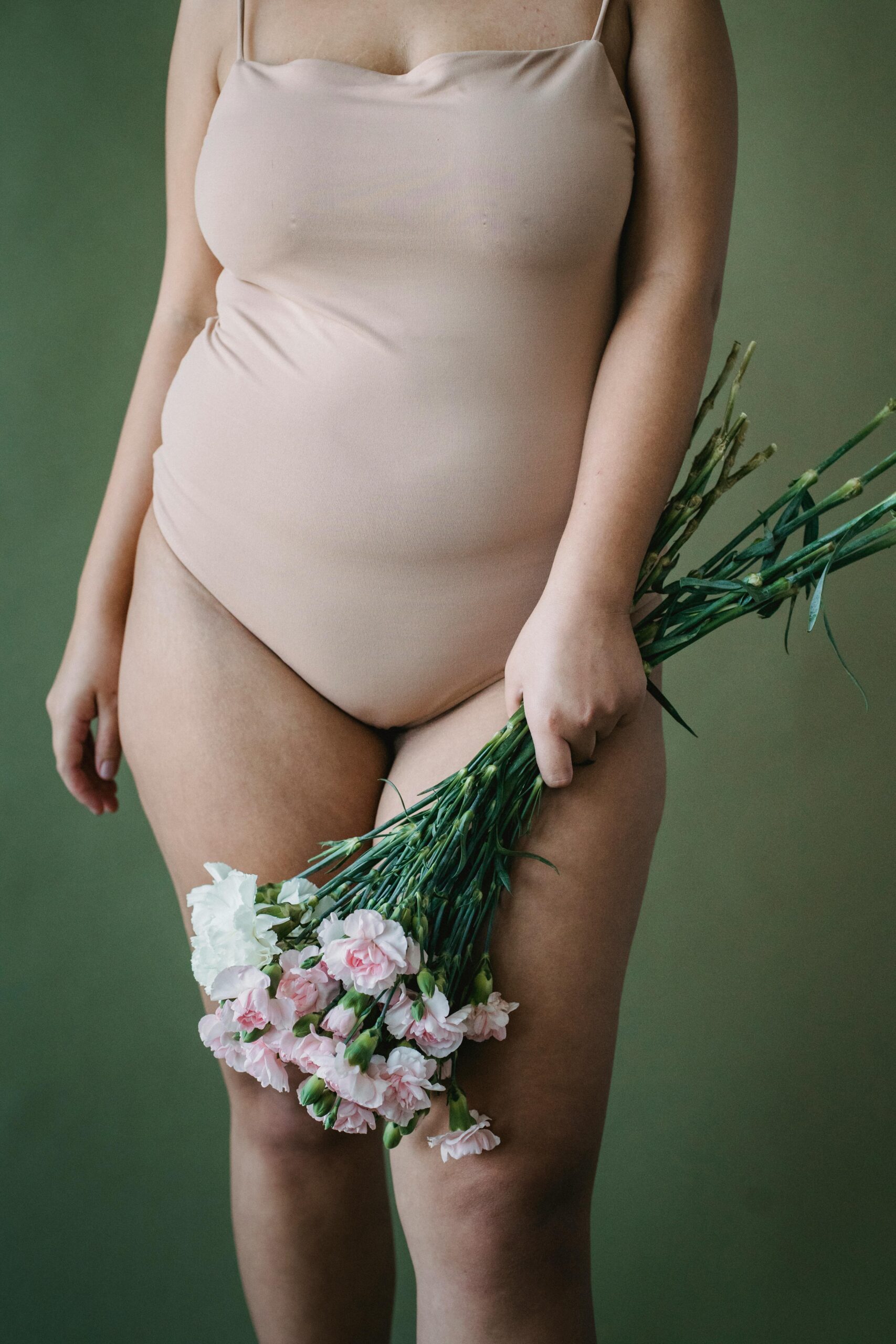 Persona con un body beige sosteniendo un ramo de flores blancas y rosas ante un fondo verde.