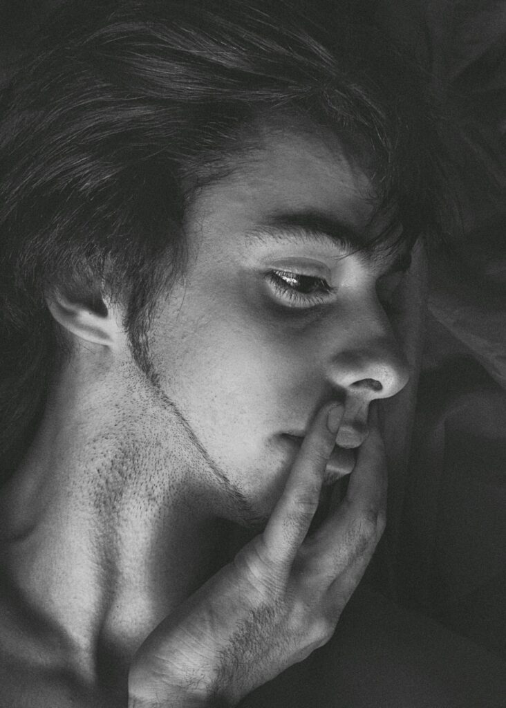 Retrato en blanco y negro de un hombre con la mirada baja y una mano junto a la boca.