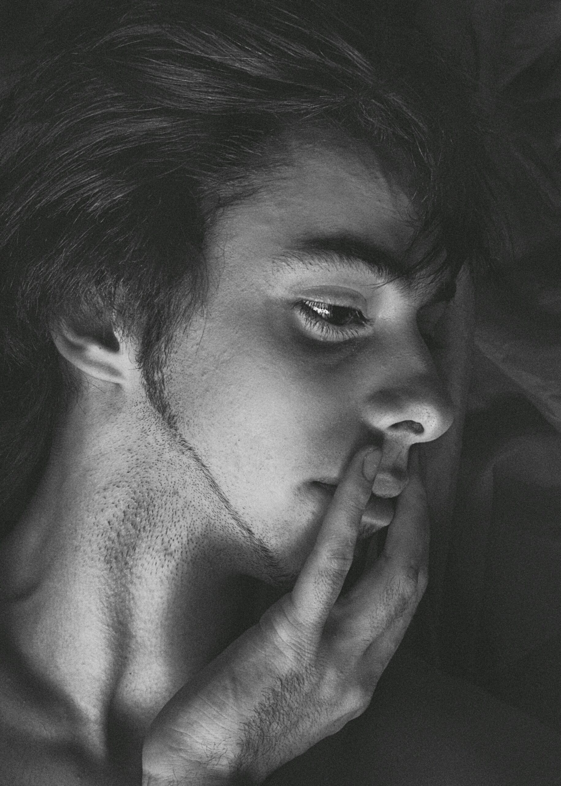 Retrato en blanco y negro de un hombre con la mirada baja y una mano junto a la boca.