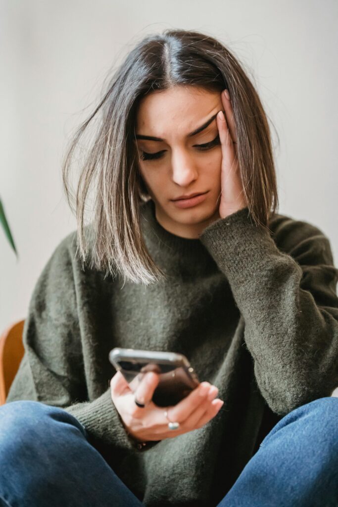 Mujer sentada mirando su teléfono móvil mientras apoya una mano en la sien.