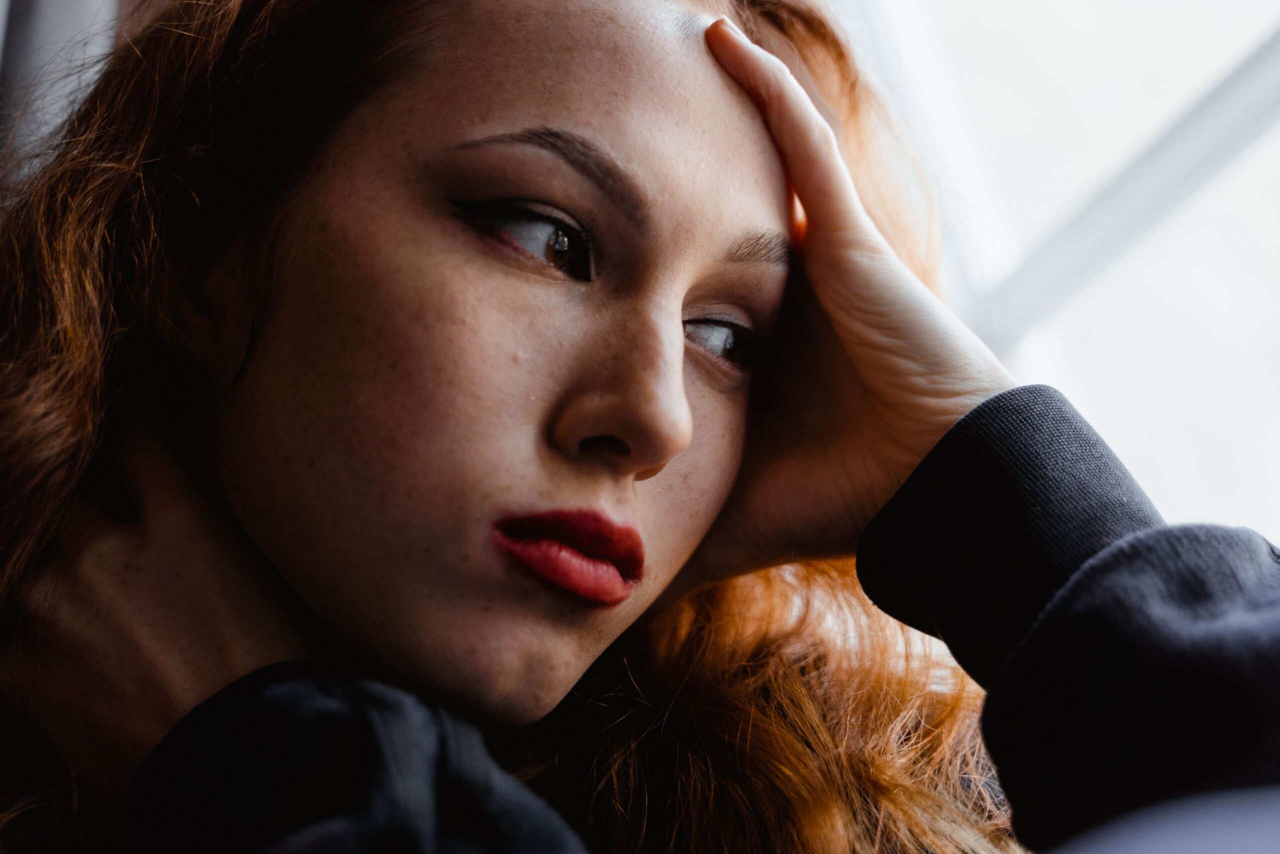 Mujer mirando por una ventana con una mano apoyada en la frente.